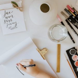A propos une expérience petie à propos : Vu du dessus sur une table blanche avec divers objets déco blancs et une main qui dessine